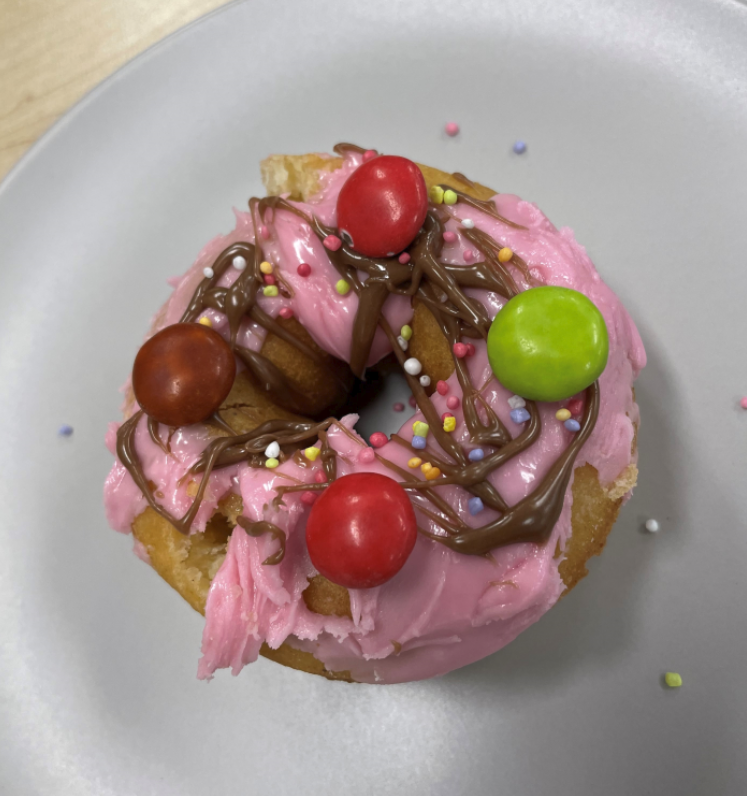 A donut decorated with pink icing, sprinkles, chocolate drizzle and smarties. Click to view full image.