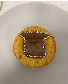 A donut decorated with chocolate icing in the shape of a slice of bread, with sprinkles used for the outline. Click to view full image.