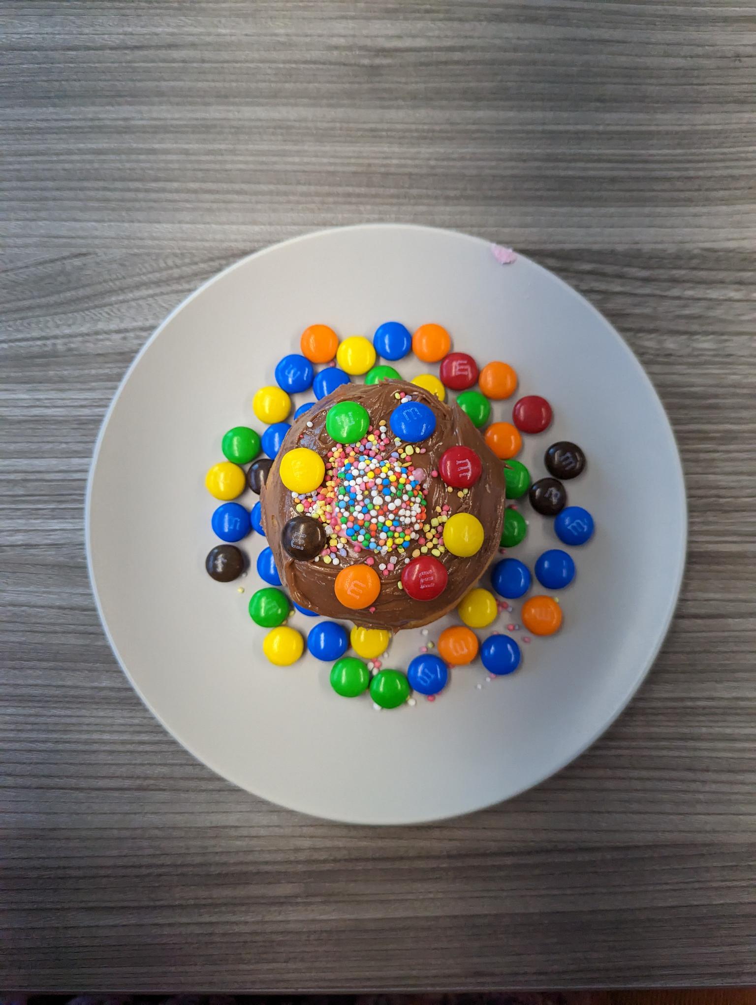 A donut decorated with sprinkles, a freckle and M&Ms. Chocolate icing is used as the base. Click to view full image.