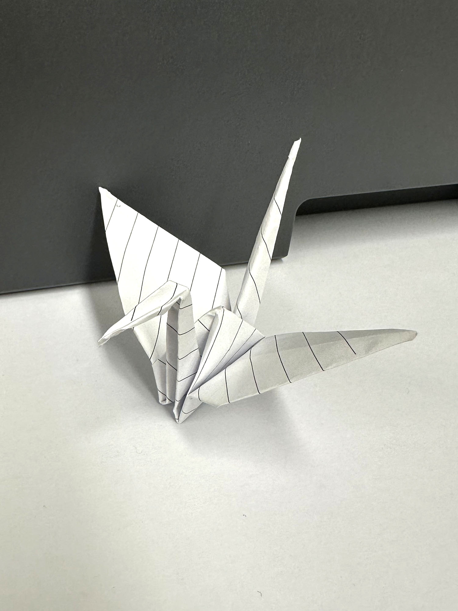 Artwork by Evelyn. An origami crane made of lined paper. Click to view full image.