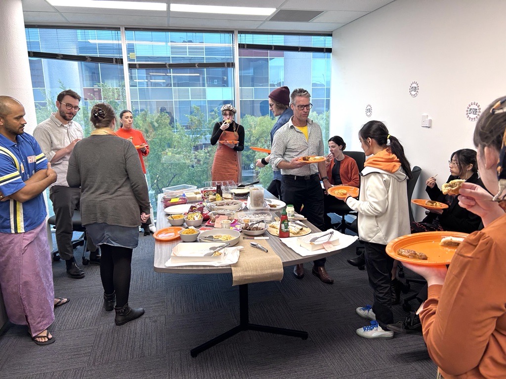 People from the Information Access Group celebrating Harmony Day. Some are collecting food from the conference table on plates and some are sitting and talking with each other. Click to view full image.